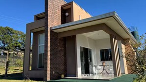 A modern two-story house with a brick facade, large windows, and a covered patio area. - Quiet family home on a gin distillery with over 80 amenities. (São João do Ivaí)