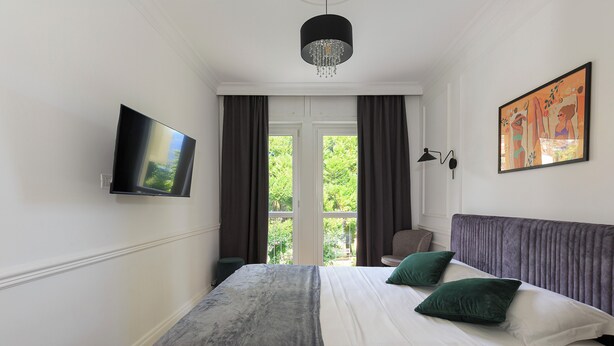 A hotel room with a bed, a television, a painting, and a window with curtains. - Sense Rooms - Joy (Baveno)