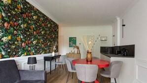 A modern living room with a red dining table, grey chairs, a grey sofa, and a floral wallpaper. - Sense Rooms - Joy (Baveno)