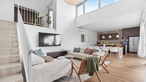 Amplia sala de estar con techo alto, una escalera, una cocina moderna y un comedor.