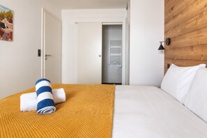 A hotel room with a bed, a wooden headboard, a white door, and a hallway leading to a bathroom. - Apartment Aiguille d'Or (Les Houches)