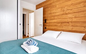 Une chambre d’hôtel avec une tête de lit en bois, un lit recouvert de draps blancs et un plaid turquoise.