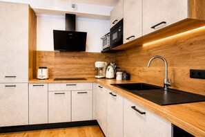 A modern kitchen with wooden cabinetry, a black countertop, a sink, a coffee maker, and a microwave. - Apartment Aiguille d'Or (Les Houches)