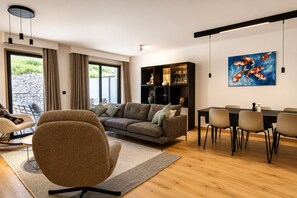 A modern living room with a grey sofa, a dining table with chairs, a bookshelf, and a painting of koi fish. - Apartment Aiguille d'Or (Les Houches)