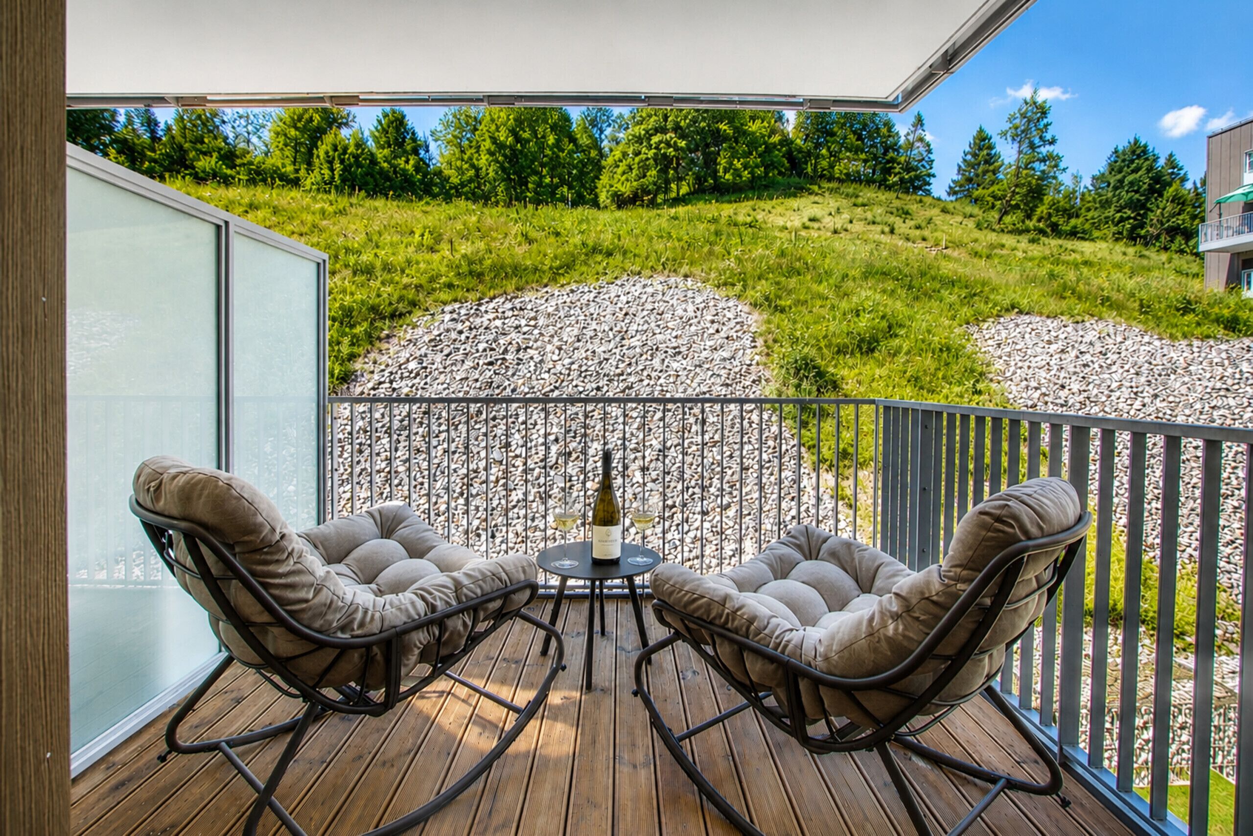 Un balcon avec deux fauteuils confortables et une petite table, donnant sur un paysage verdoyant avec une zone rocheuse.