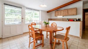 Un coin repas avec une table et des chaises en bois, une cuisine avec des meubles en bois et une vue dégagée sur l’extérieur grâce à de grandes fenêtres.