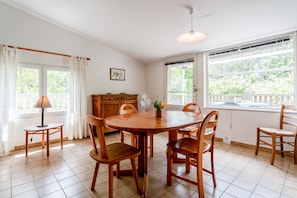 En matplats med ett runt träbord, sex trästolar, ett litet sidobord med en lampa, en fläkt och en dekorativ vas med blommor.