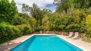Une piscine rectangulaire à l’eau d’un bleu limpide, entourée d’un mur de pierre et d’une végétation luxuriante.