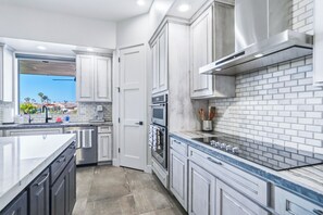 Una cocina moderna con armarios blancos, una isla grande y vistas a palmeras al exterior.