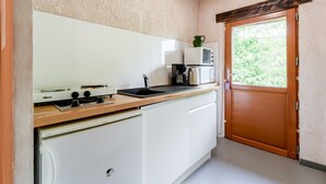 Een compacte keuken met een kookplaat, magnetron en spoelbak, een houten aanrechtblad en een deur naar een tuin.