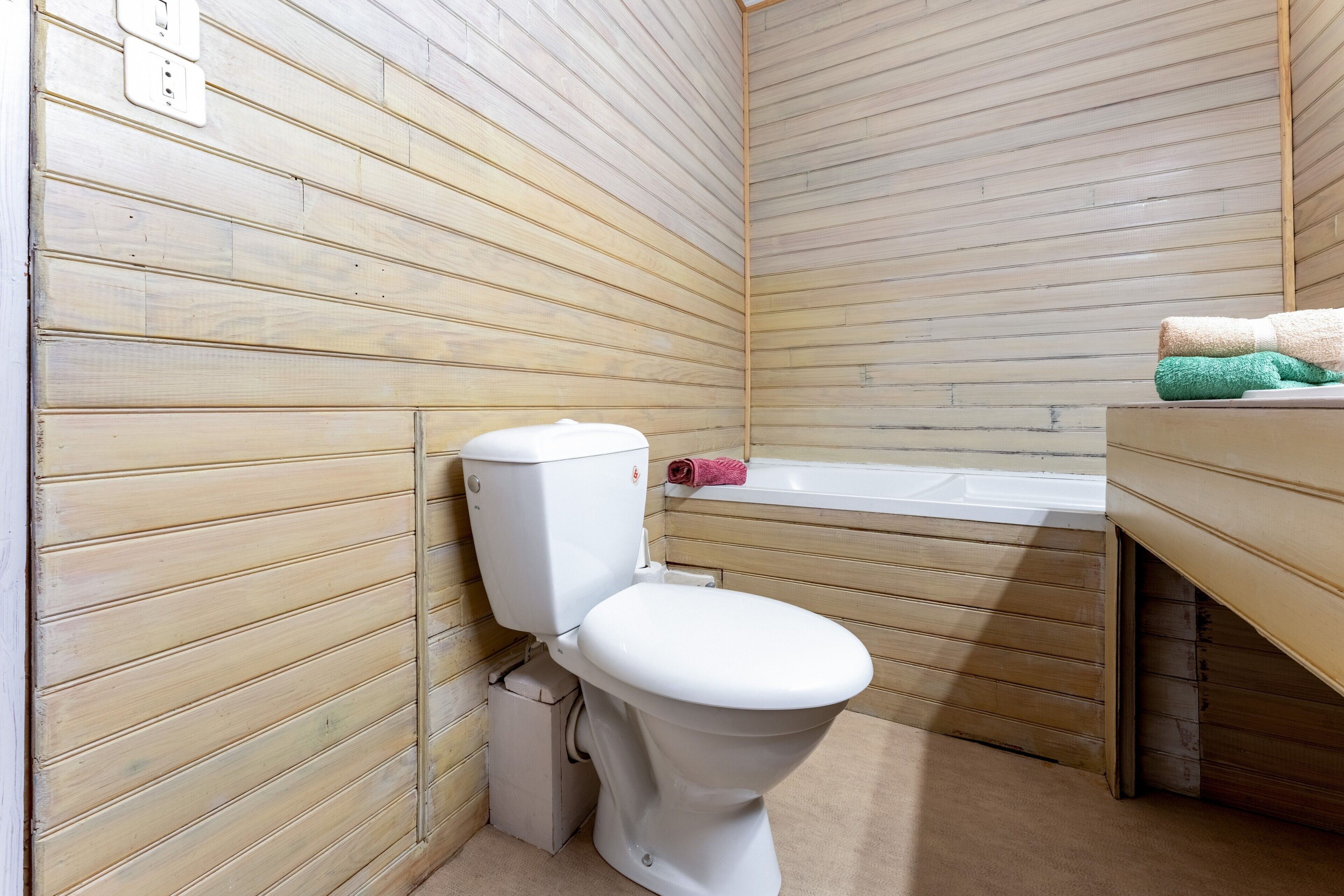 Un baño con paneles de madera, un inodoro blanco, una bañera y un lavabo con toallas.