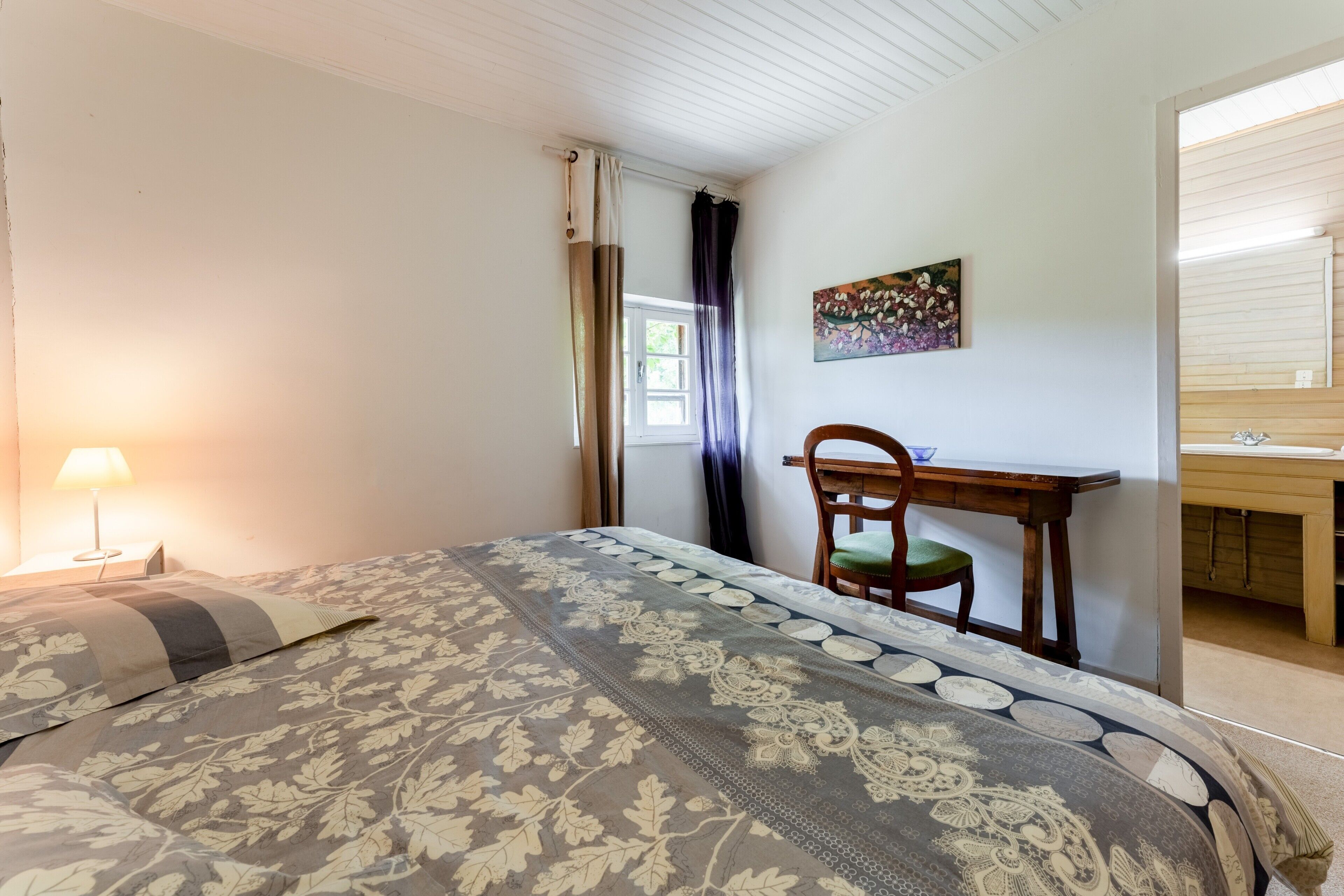 Une chambre à coucher avec un lit, un bureau, une chaise, une lampe et un tableau au mur.