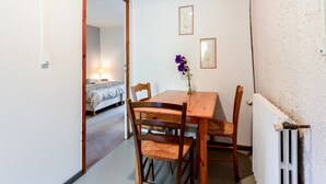 Een gezellig eetgedeelte met een houten tafel en stoelen, een vaas met bloemen, en een bed in de aangrenzende kamer.