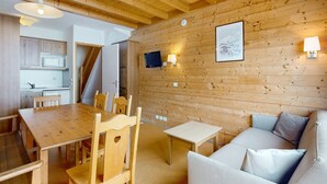 Un acogedor interior de cabaña con una mesa de comedor de madera, sillas, un sofá y un televisor montado en la pared.