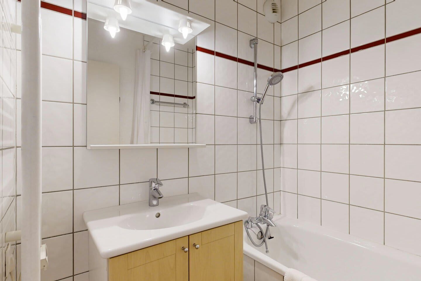 Un baño moderno con un lavabo blanco, un mueble de madera y una ducha con cabezal de ducha manual.