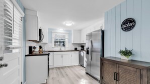 A modern kitchen with white cabinets, a stainless steel refrigerator, and a wooden cabinet with a plant. - Sea Breeze Retreat (North Myrtle Beach)