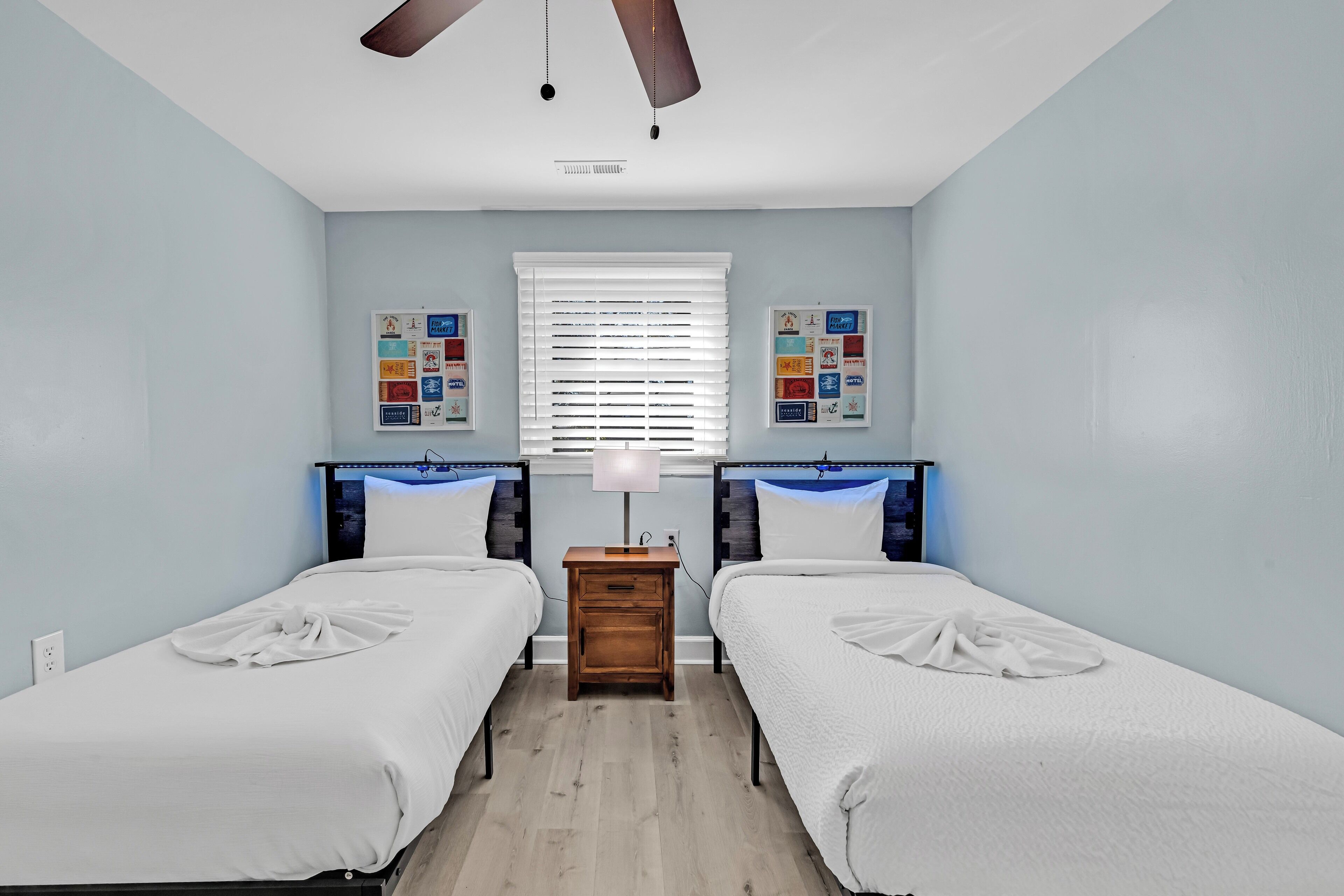 A bedroom with two single beds, a nightstand, a ceiling fan, and a window with blinds.