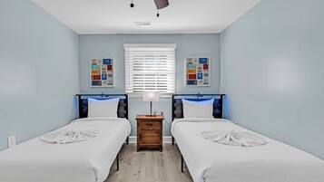 A bedroom with two single beds, a nightstand, a ceiling fan, and a window with blinds.