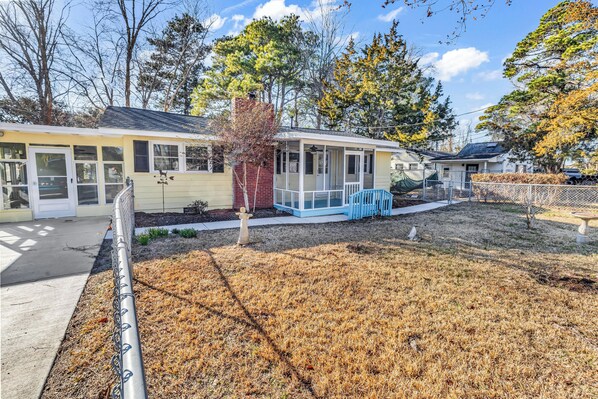 A single-story building with a covered porch, a fenced yard, and a small tree. - Sea Breeze Retreat (North Myrtle Beach)