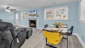 A living room with a fireplace, a dining table with yellow chairs, and a grey sofa. - Sea Breeze Retreat (North Myrtle Beach)