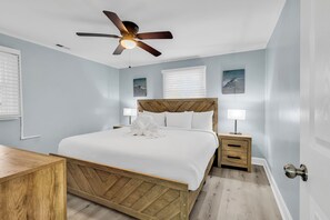 A bedroom with a wooden bed, a ceiling fan, a nightstand, and a bedside table. - Sea Breeze Retreat (North Myrtle Beach)
