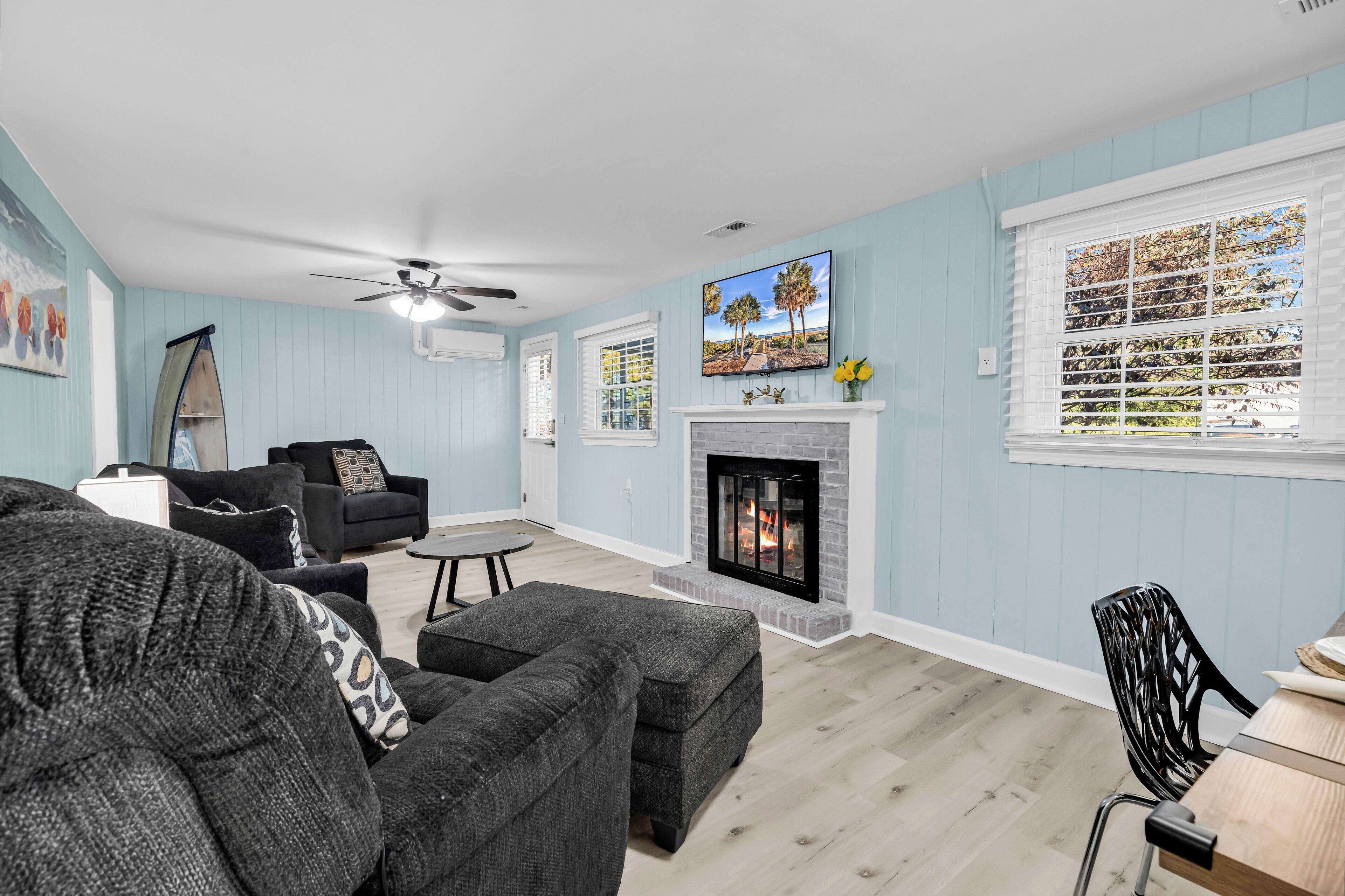 A living room with a fireplace, a ceiling fan, and a TV mounted on the wall.