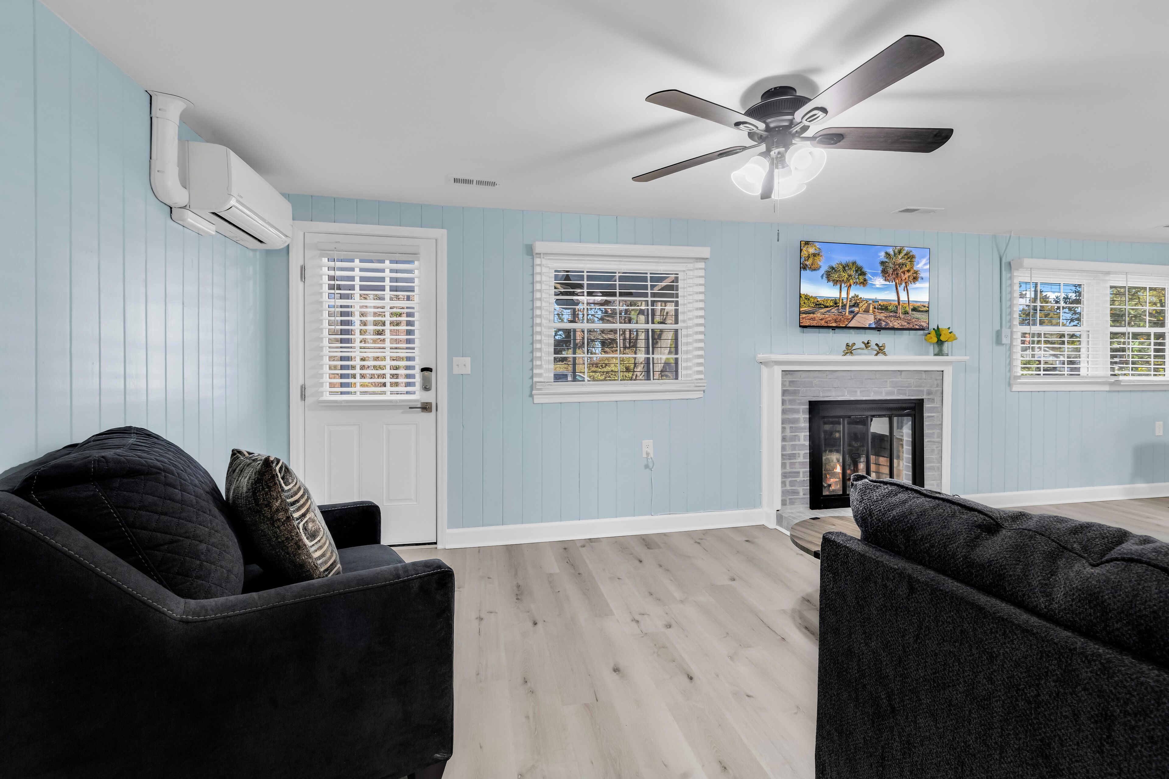A living room with a ceiling fan, a fireplace, and a large window with blinds.