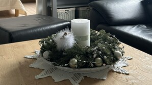 Ein Wohnzimmer mit einem Holztisch, einem schwarzen Ledersofa, einer grauen Kommode und einem armchair mit floralem Muster.