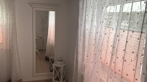 Ein Zimmer mit Holzboden, einem Spiegel, einer kleinen Laterne und durchscheinenden Vorhängen mit Blumenmuster.