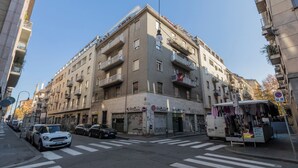 Um edifício de vários andares com varandas, uma loja no rés-do-chão e uma passadeira para peões.