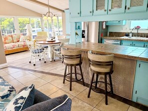 A modern kitchen with a central island, bar stools, and a dining area with a sofa and chairs. - Cozy 1-bedroom cottage in gorgeous Jensen Beach gated community (Jensen Beach)