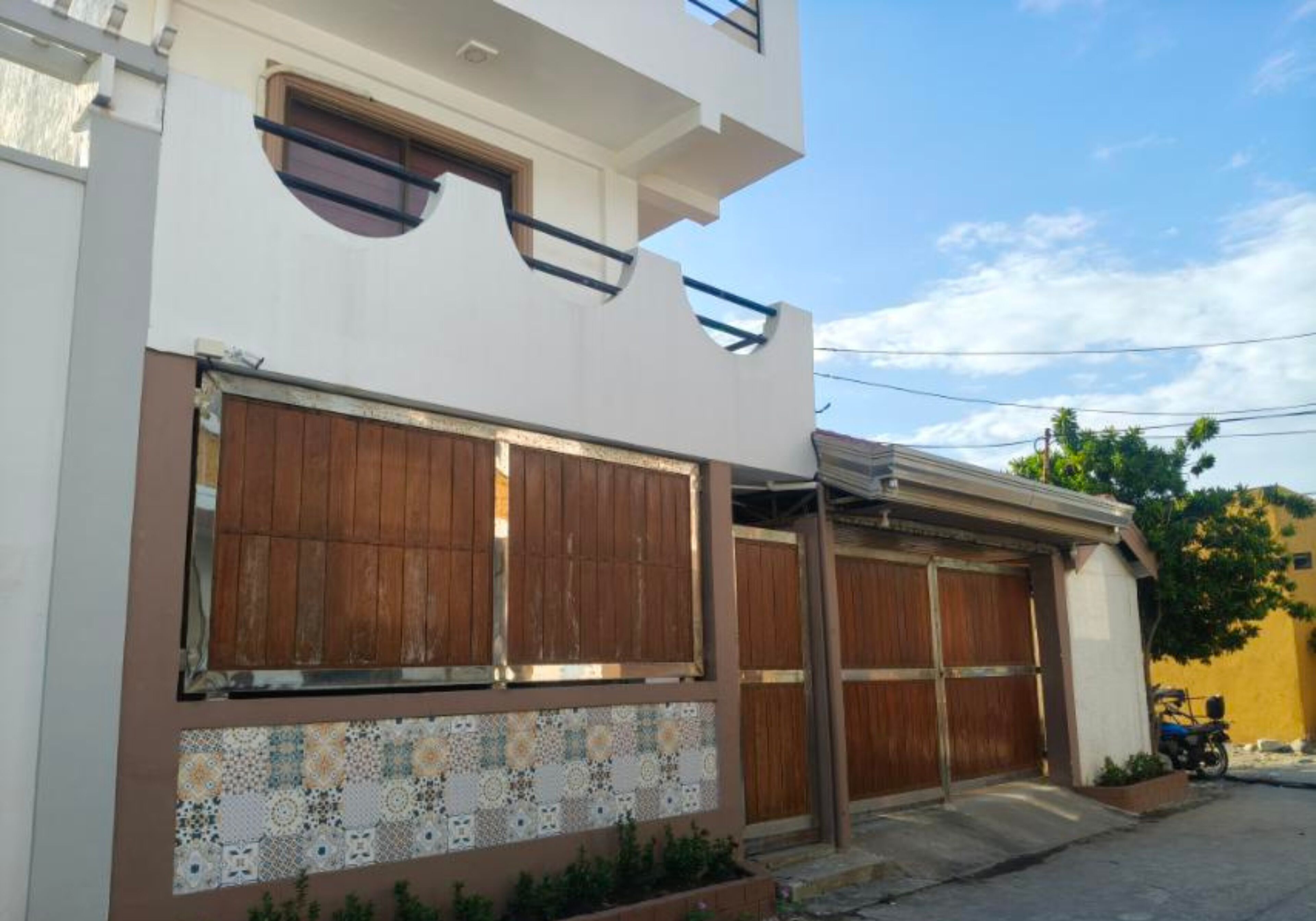 Un edificio de dos plantas con fachada blanca, grandes puertas de garaje de madera y una sección inferior revestida con baldosas.