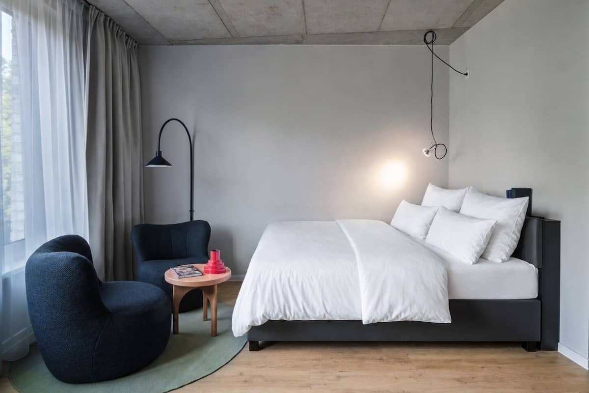 A modern bedroom with a bed, a chair, a small table, and a lamp.