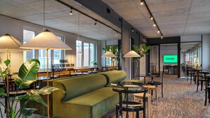 A modern interior with a green sofa, round tables, and large windows.