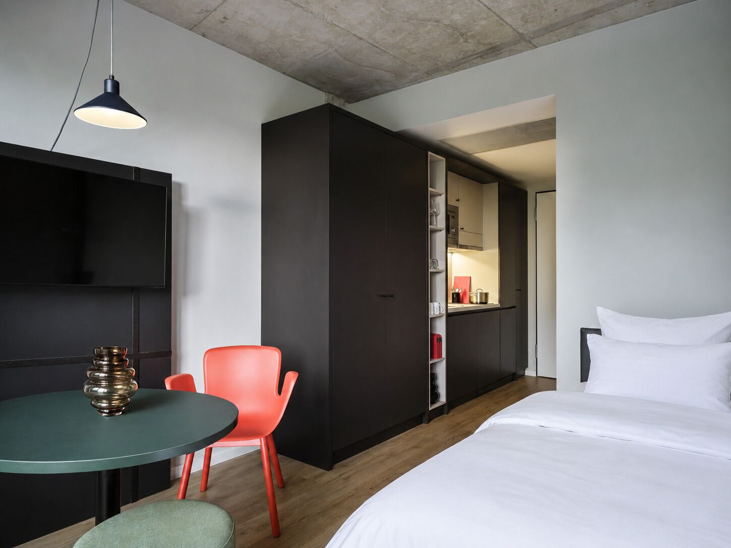 Een moderne hotelkamer met een bed, een eettafel met stoelen, een televisie en een kitchenette.