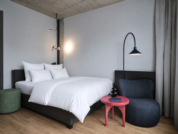 A modern hotel room with a bed, a chair, a small table, a lamp, and a wall-mounted light fixture. - STAYERY Bremen Altstadt (Bremen)