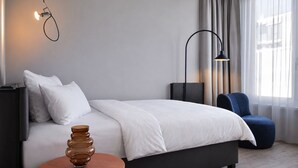 A modern hotel room with a bed, bedside table, lamp, and a view of the outside.