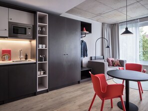 A modern kitchen with a built-in microwave, a sink, and open shelving. There is a dining area with a round table and red chairs. A sofa and a lamp are visible in the background. - STAYERY Bremen Altstadt (Bremen)