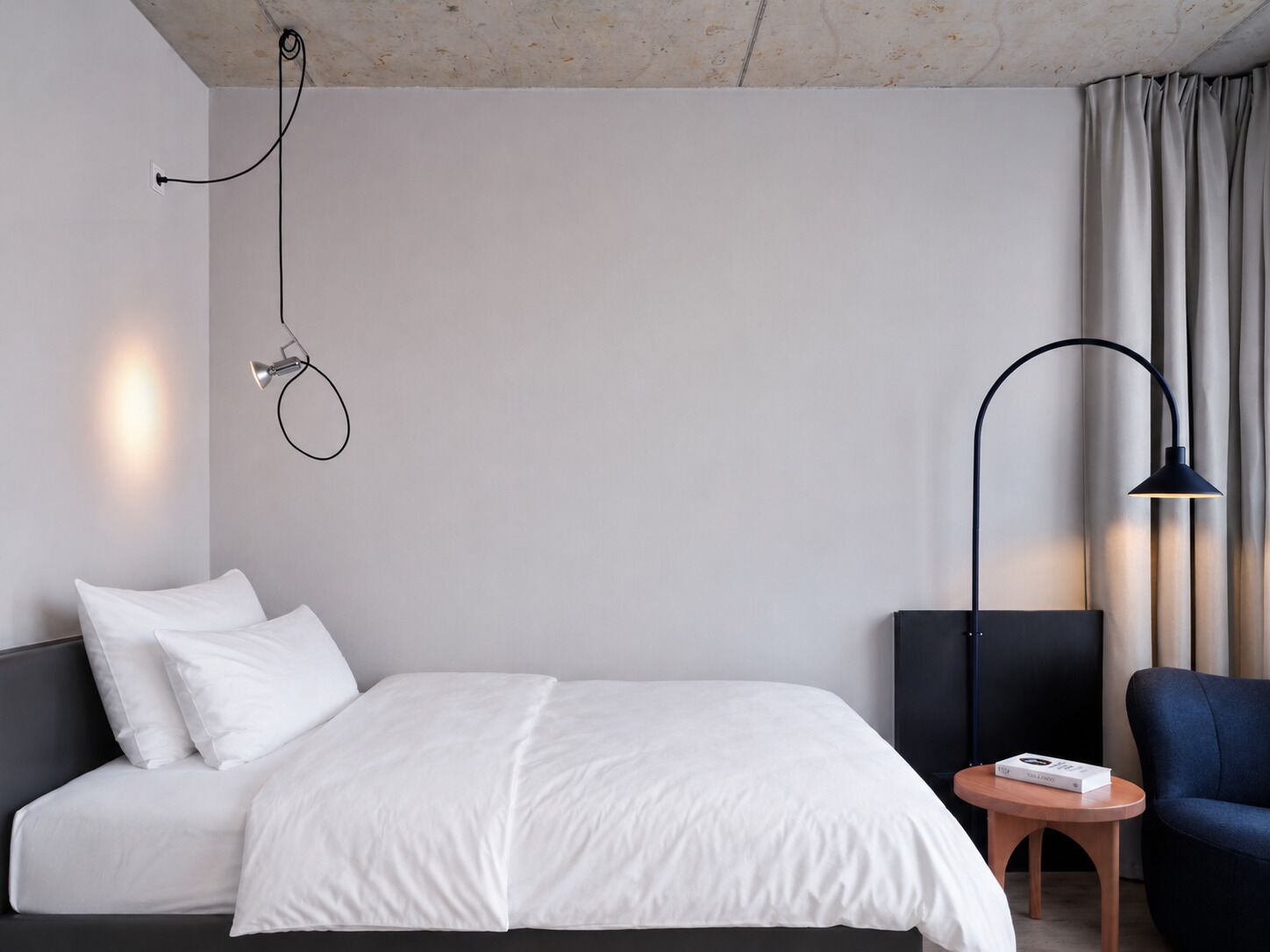A modern hotel room with a bed, a desk, a chair, and a lamp.