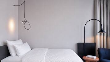 A modern hotel room with a bed, a desk, a chair, and a lamp.