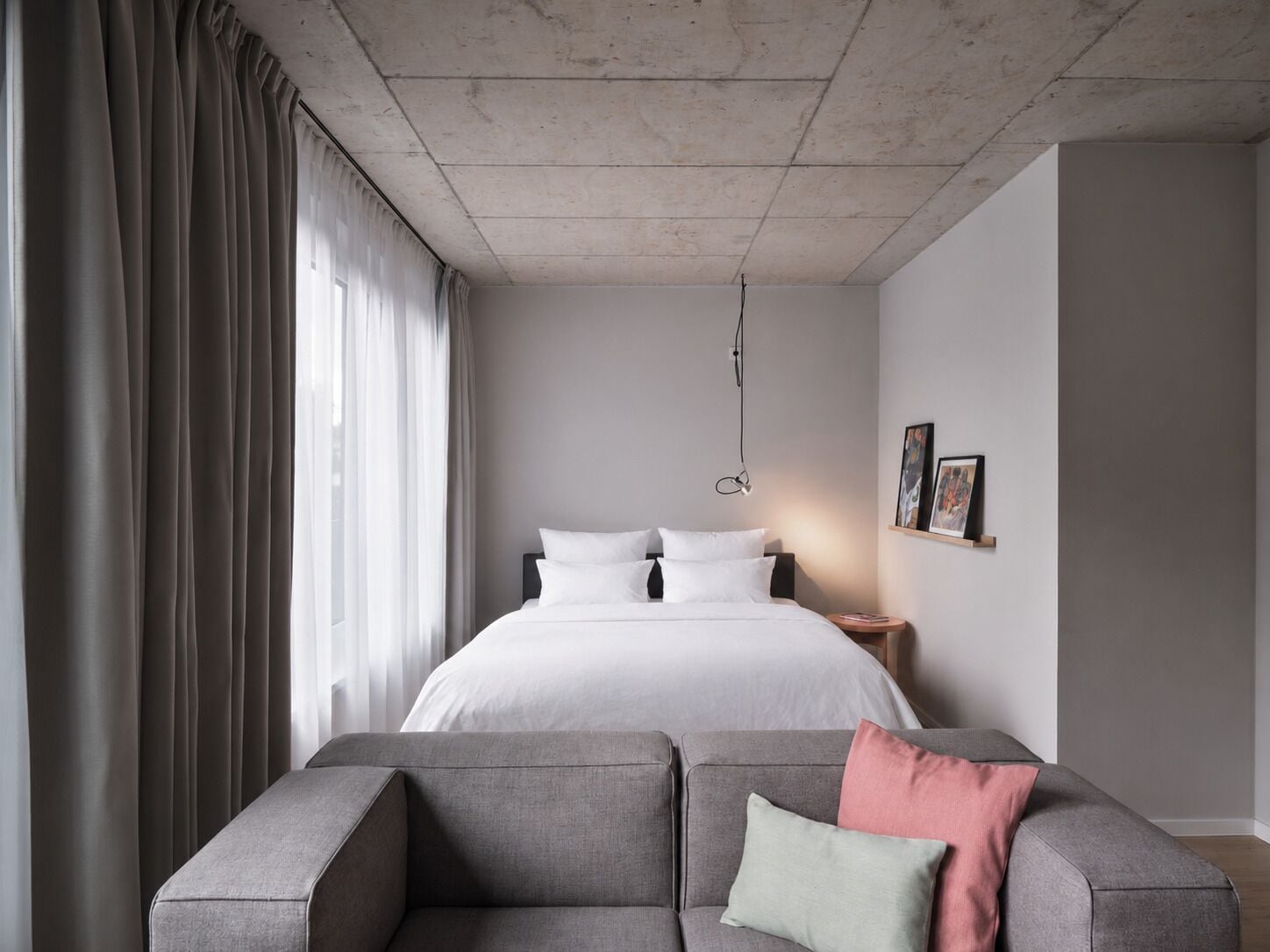 A modern bedroom with a large bed, grey sofa, and a bedside table with a lamp.