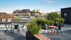 A rooftop terrace with outdoor seating, greenery, and a city view.