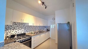 A modern kitchen with white cabinets, a black stove, a stainless steel sink, and a refrigerator. - Spacious 2BR | Apt Private Baths | Near PC Airport (Punta Cana)