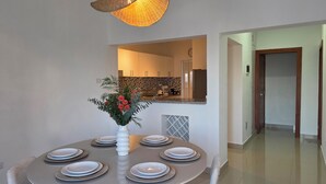 A dining area with a round table set for six, a vase of flowers, and a kitchen in the background. - Spacious 2BR | Apt Private Baths | Near PC Airport (Punta Cana)