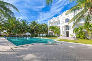 A resort with a swimming pool, palm trees, and a large white building with multiple balconies.