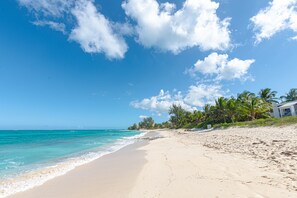 Una playa con agua turquesa cristalina, una orilla arenosa y una hilera de palmeras.
