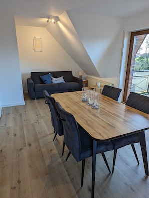A dining area with a wooden table and chairs, a sofa with cushions, and a ceiling light fixture.