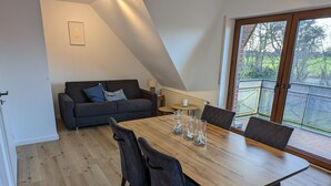 A dining area with a wooden table, four chairs, and a sofa with pillows. - Apartment 'Am Meer Nordsee' with Shared Garden, Balcony & Wi-Fi (Wangerland)