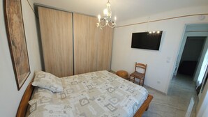 A bedroom with a bed, a wooden wardrobe, a television, and a chair. - DETACHED BUNGALOW AT THE BACK OF OUR 2-STAR VILLA (Fréjus)