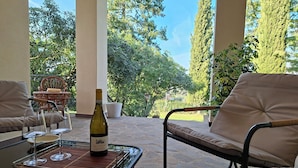 Um pátio com mesa de vidro, duas cadeiras acolchoadas, uma garrafa de vinho e copos de vinho.